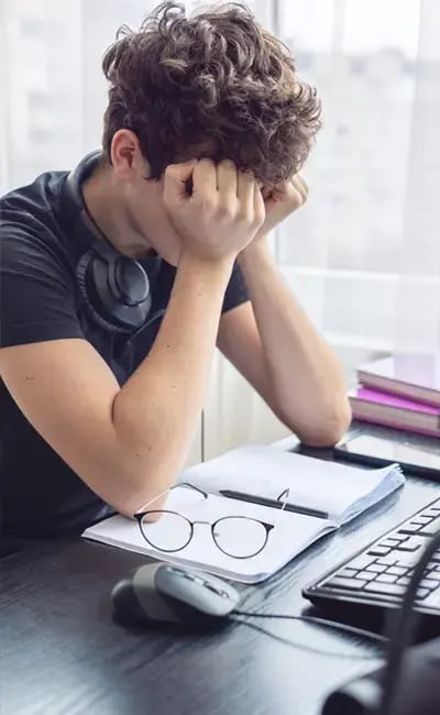 an upset boy at computer with his hands over his face.
